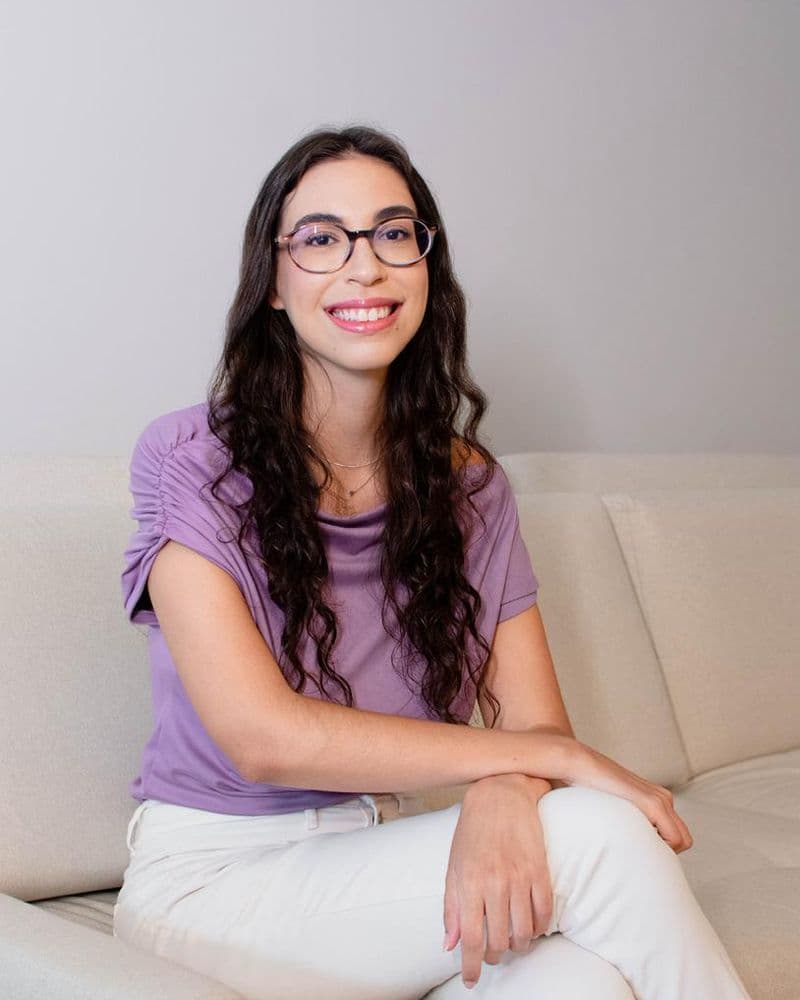 Psicóloga Bianca Correa sorrindo no sofá, pronta para a terapia online